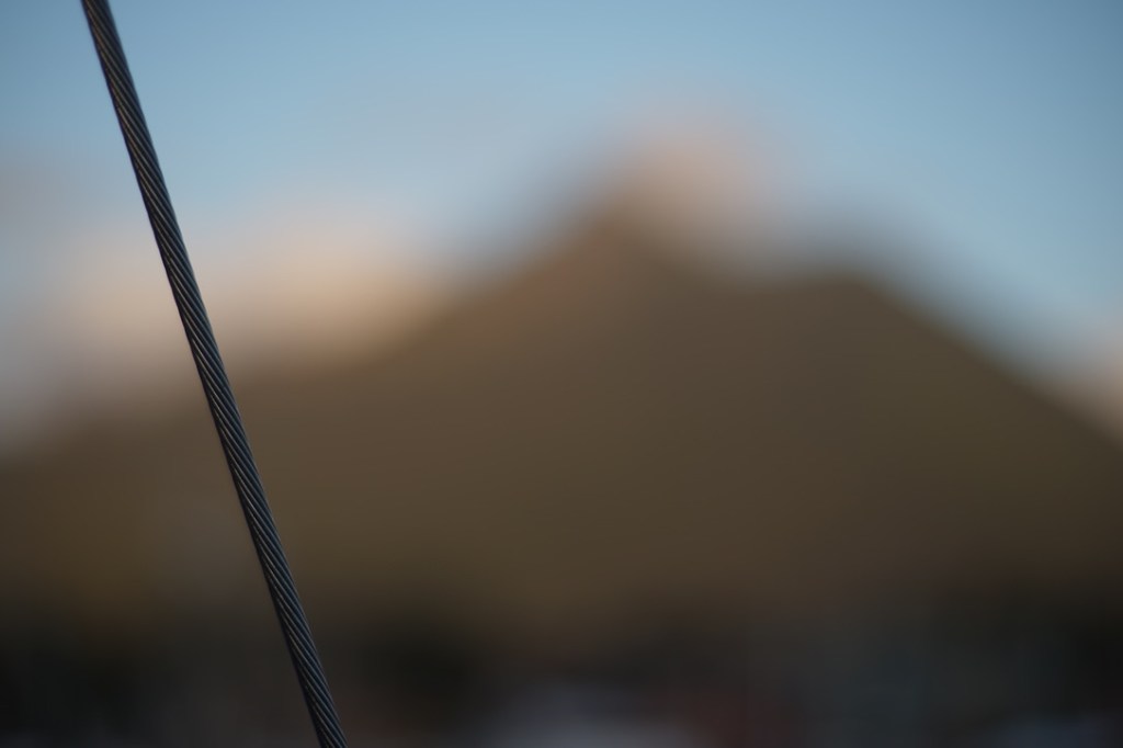 a steel line is in focus and in the foreground. behind it, all blurred from focus, a blue sky, a mountain, perhaps covered in trees.