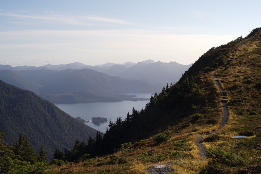 a small path winds gently along an alpine ridgeline, the grasses going golden in the Fall sun. Next to this path, next to this ridgeline, evergreen soaked mountains sprawl into the sea.